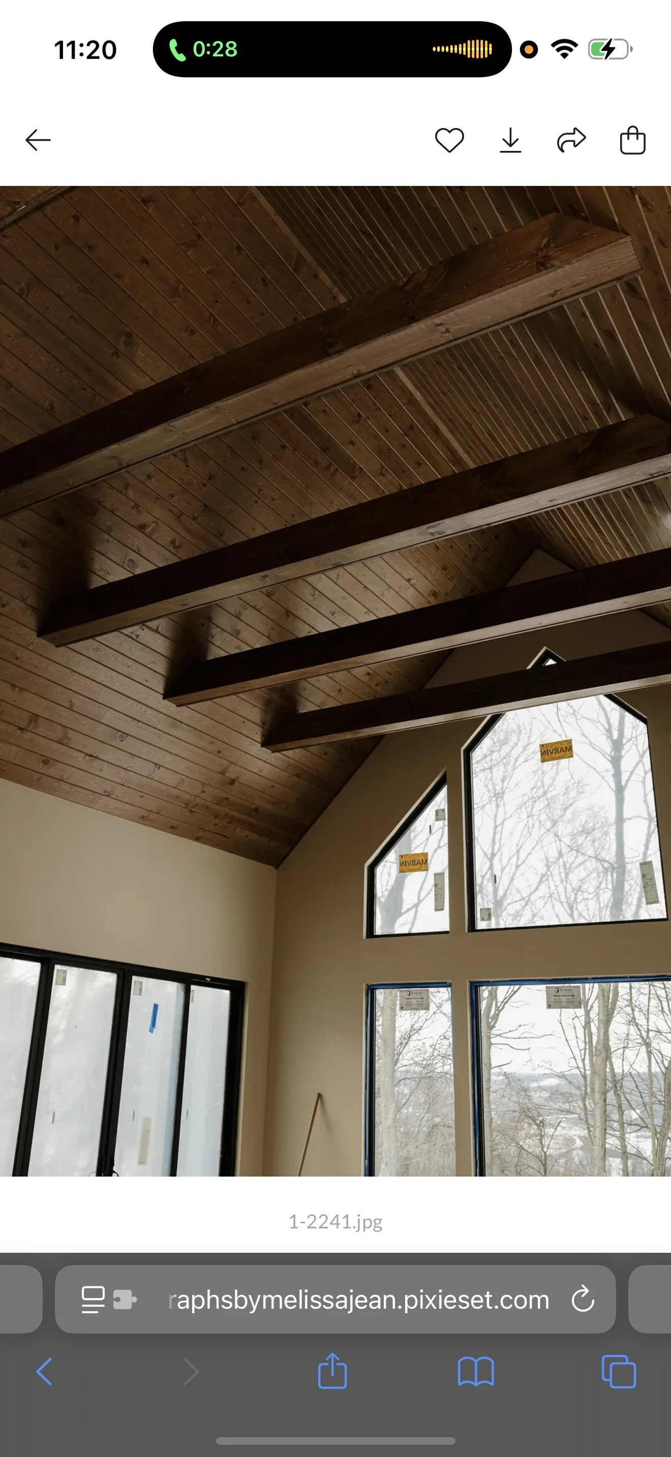 Vaulted ceiling with dark exposed beams, wood paneling, and cream painted walls with large windows