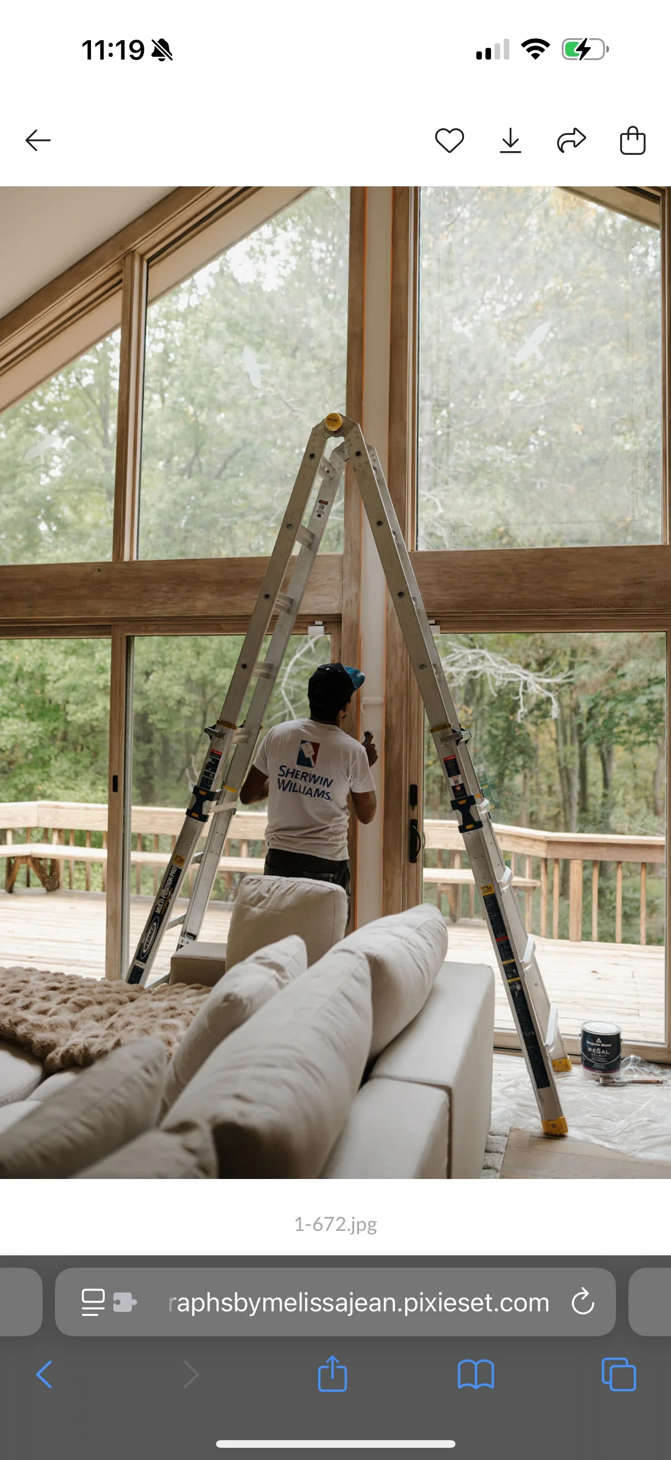 Painter on ladder applying paint to interior window trim and frames with wood molding